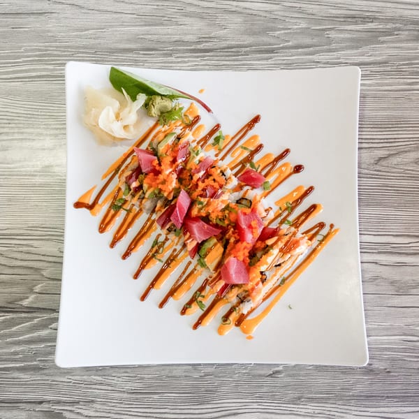 Sushi rolls topped with tuna, avocado, and roe, drizzled with sauces on a white plate.