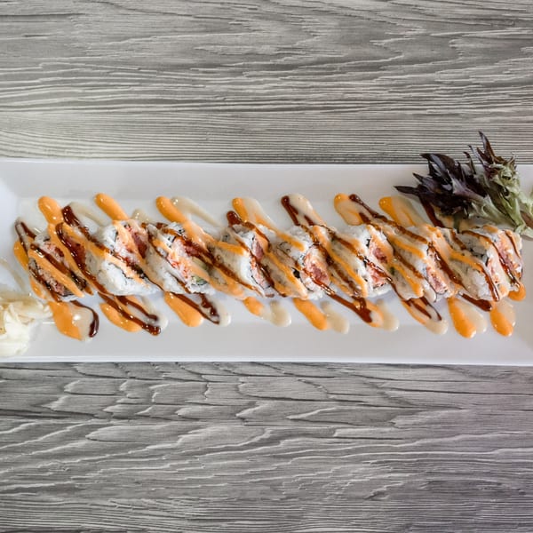 Sushi roll with spicy mayo and eel sauce drizzle, garnished with pickled ginger and greens.