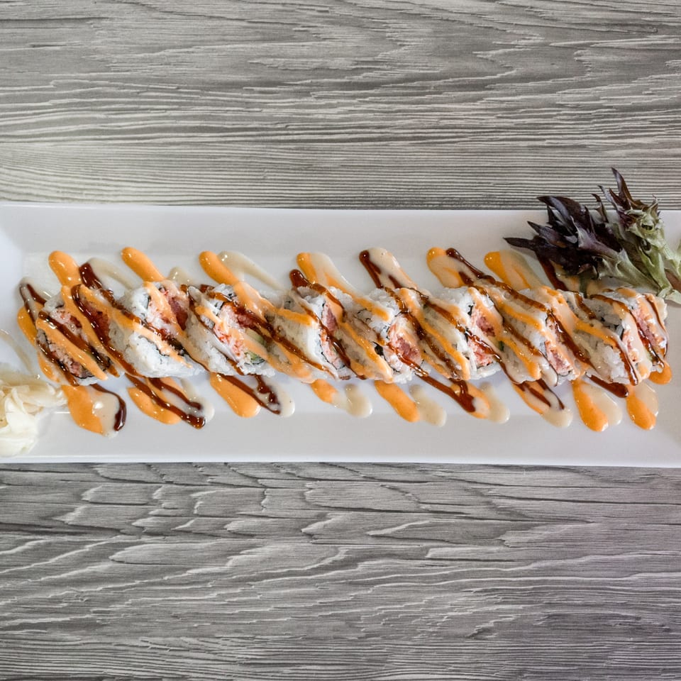 Sushi roll with spicy mayo and eel sauce drizzle, garnished with pickled ginger and greens.