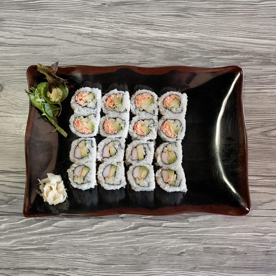 California rolls with avocado, crab, and cucumber, served with ginger and wasabi on a dark plate.