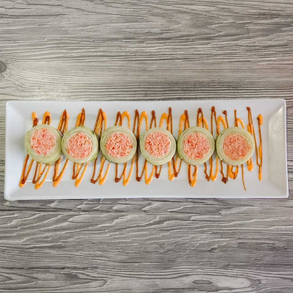 Six sushi rolls with pink filling and green wraps, drizzled with orange sauce on a white plate.